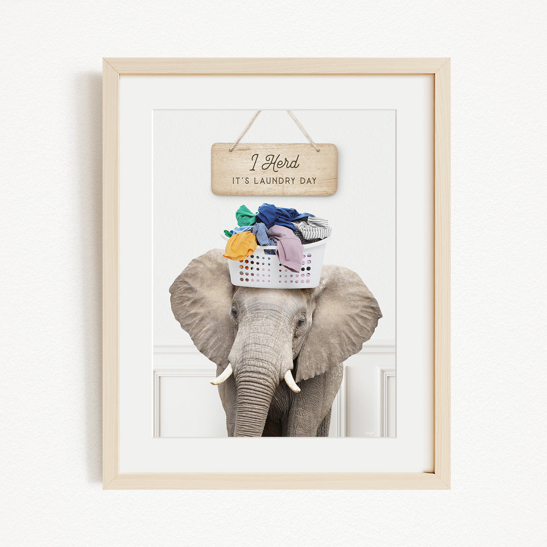 A framed image of an elephant holding a basket of laundry, with a wooden sign above it that says "I Harded it's laundry day".