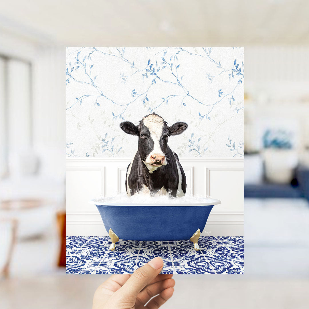 A black and white cow is sitting in a blue bathtub filled with water, surrounded by a blue and white patterned floor.
