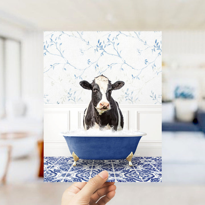 A black and white cow is sitting in a blue bathtub filled with water, surrounded by a blue and white patterned floor.