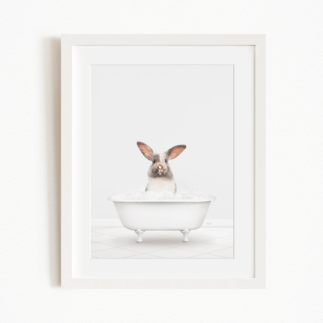 A white rabbit sitting in a white bathtub filled with bubbles, looking directly at the camera.