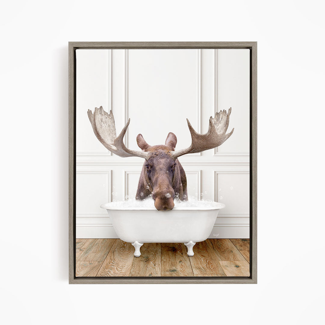A moose with large antlers is sitting in a white bathtub, appearing to enjoy the bath.