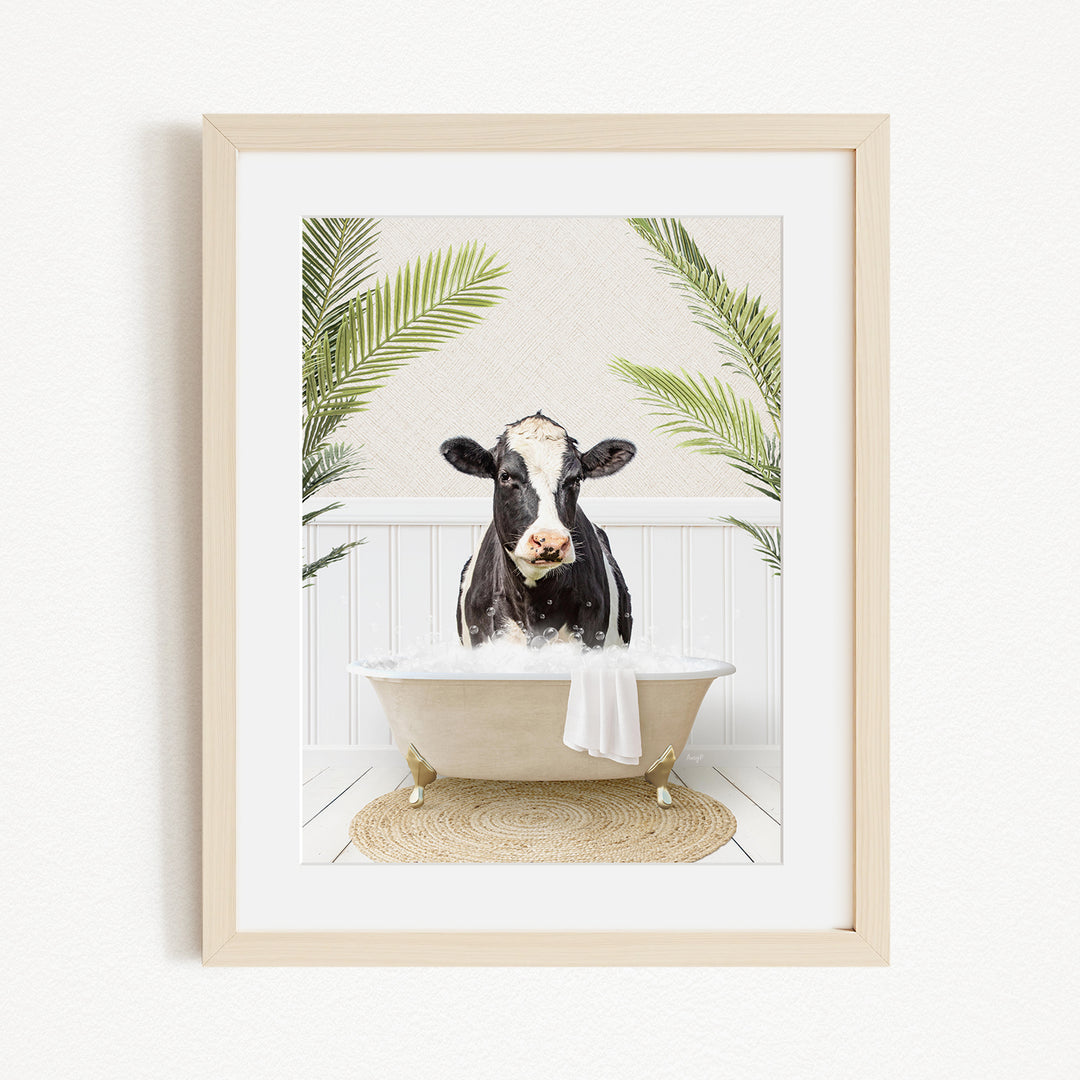 A black and white cow is sitting in a bathtub filled with water, surrounded by green palm leaves.