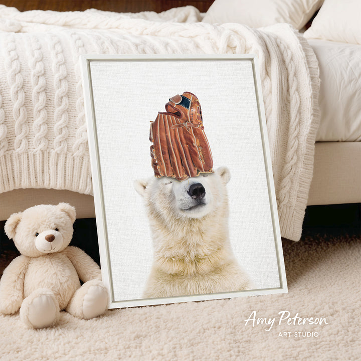 A framed photograph of a polar bear wearing a baseball glove on its head, with a teddy bear sitting next to it on a bed.