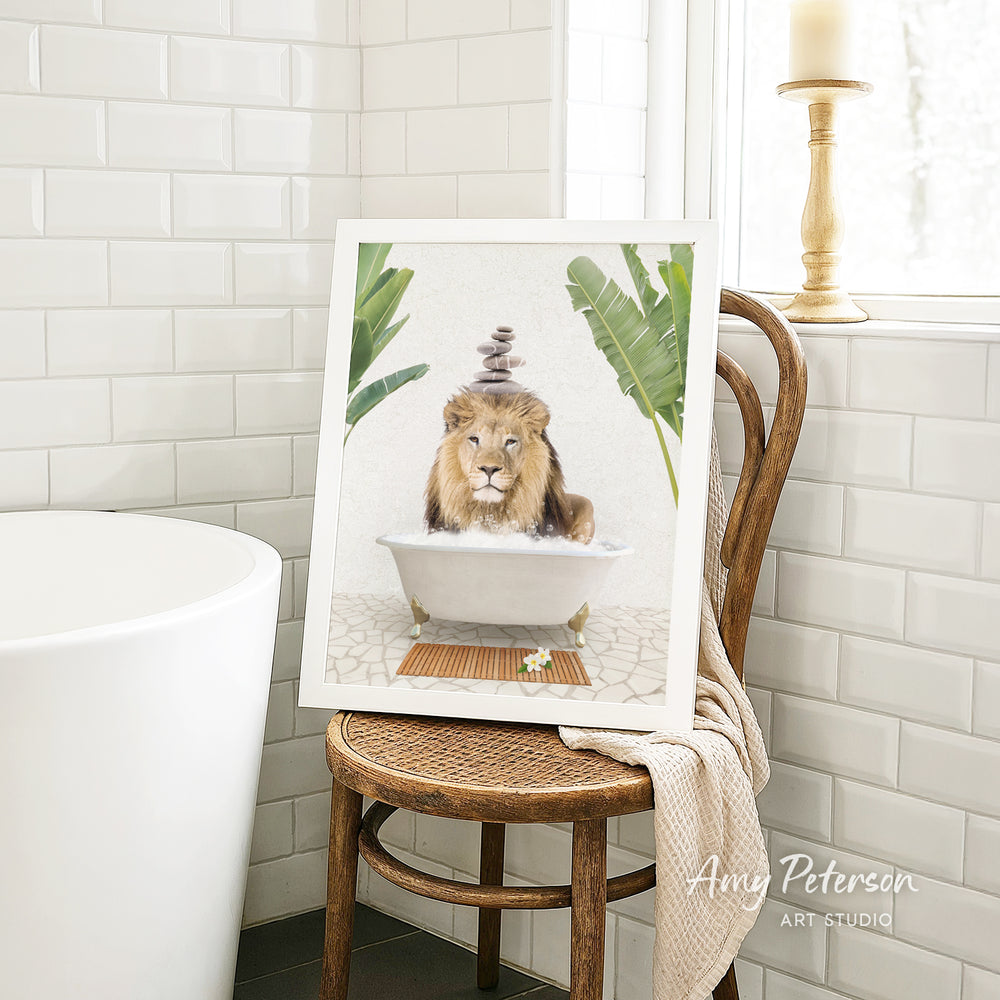 A framed image of a lion sitting in a bathtub, surrounded by tropical plants, is displayed on a wooden chair in a bathroom setting.
