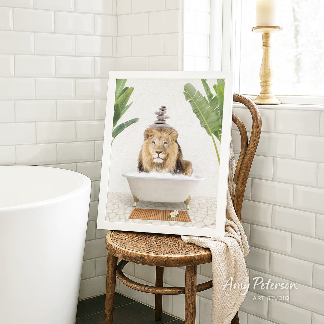 A framed image of a lion sitting in a bathtub, surrounded by tropical plants, is displayed on a wooden chair in a bathroom setting.