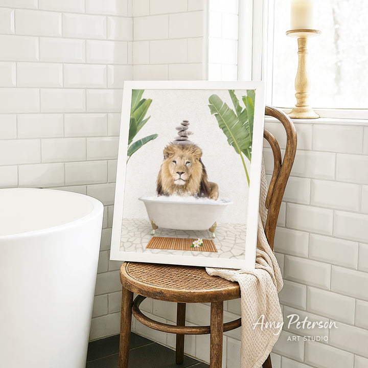 A framed image of a lion sitting in a bathtub, surrounded by tropical plants, is displayed on a wooden chair in a bathroom setting.
