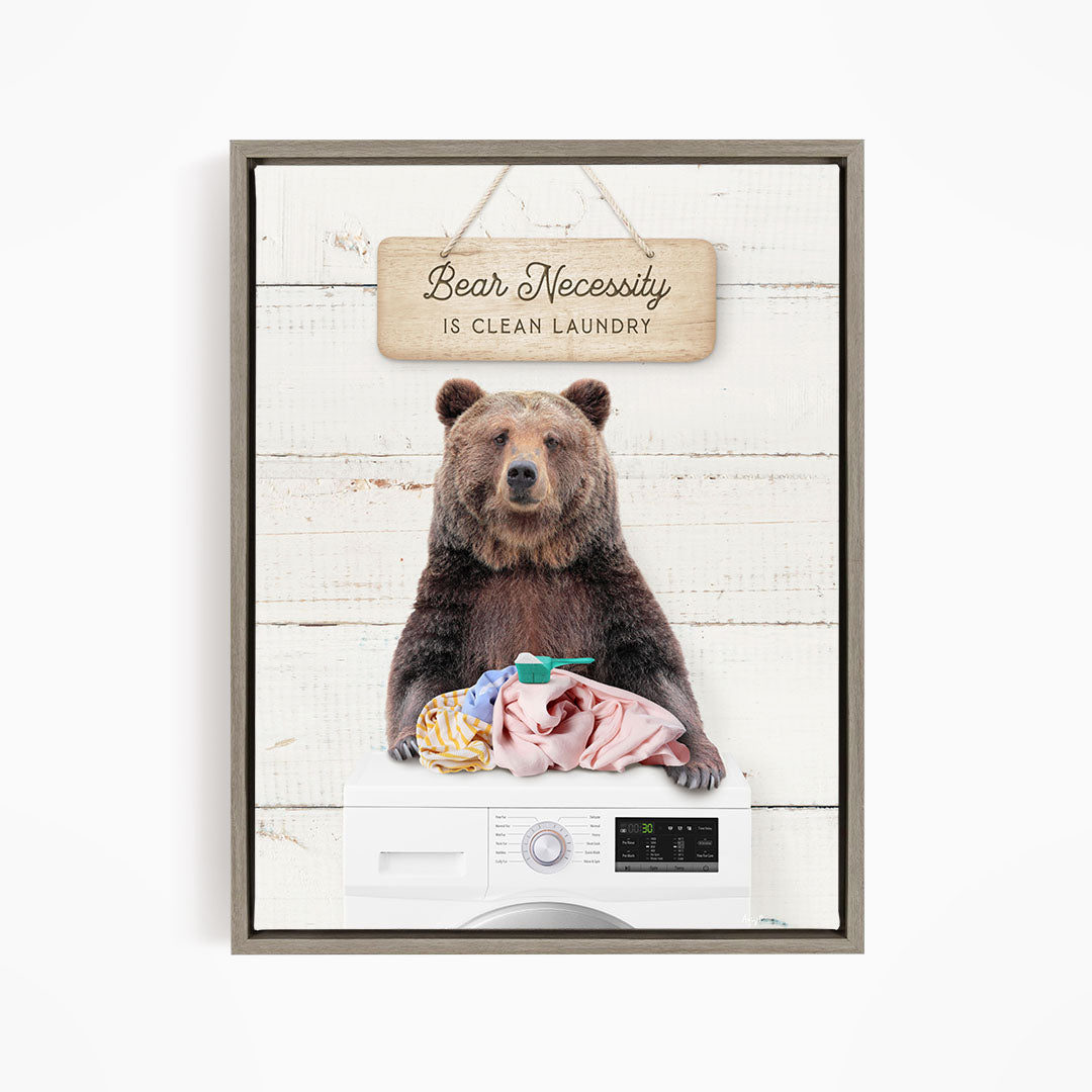 A brown bear sitting on top of a washing machine, with a sign above that says "Bear Necessity is Clean Laundry".