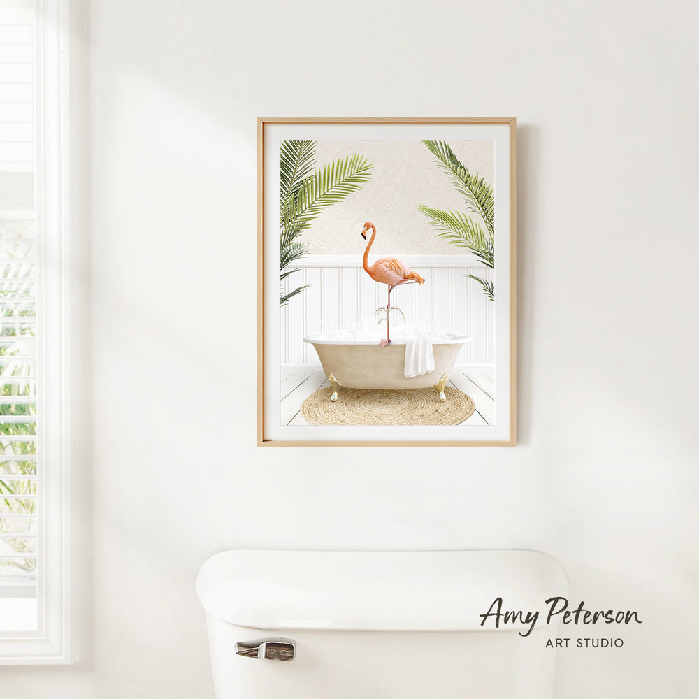 A framed print of a flamingo standing in a bathtub, surrounded by palm leaves, hangs on a white wall in a bathroom.