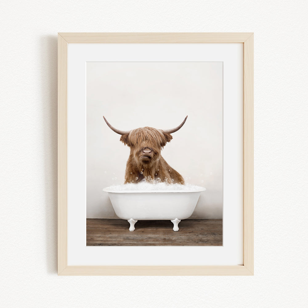 A brown Highland cow with long horns is sitting in a white bathtub filled with water, creating a whimsical and playful scene.