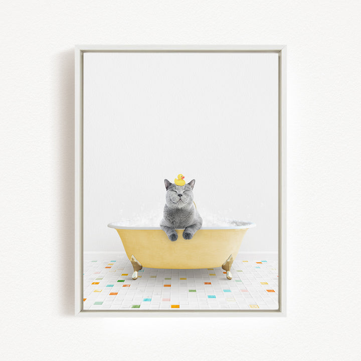 A gray cat sitting in a yellow bathtub filled with bubbles, wearing a yellow hat.