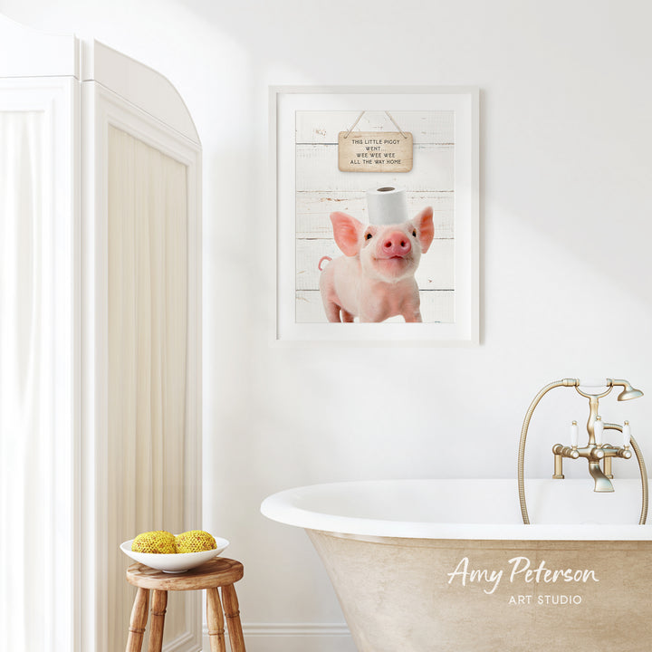 a bathroom with a framed picture of a pig wearing a toilet paper hat, a wooden stool with a bowl of fruit, and a white bathtub with a gold faucet.