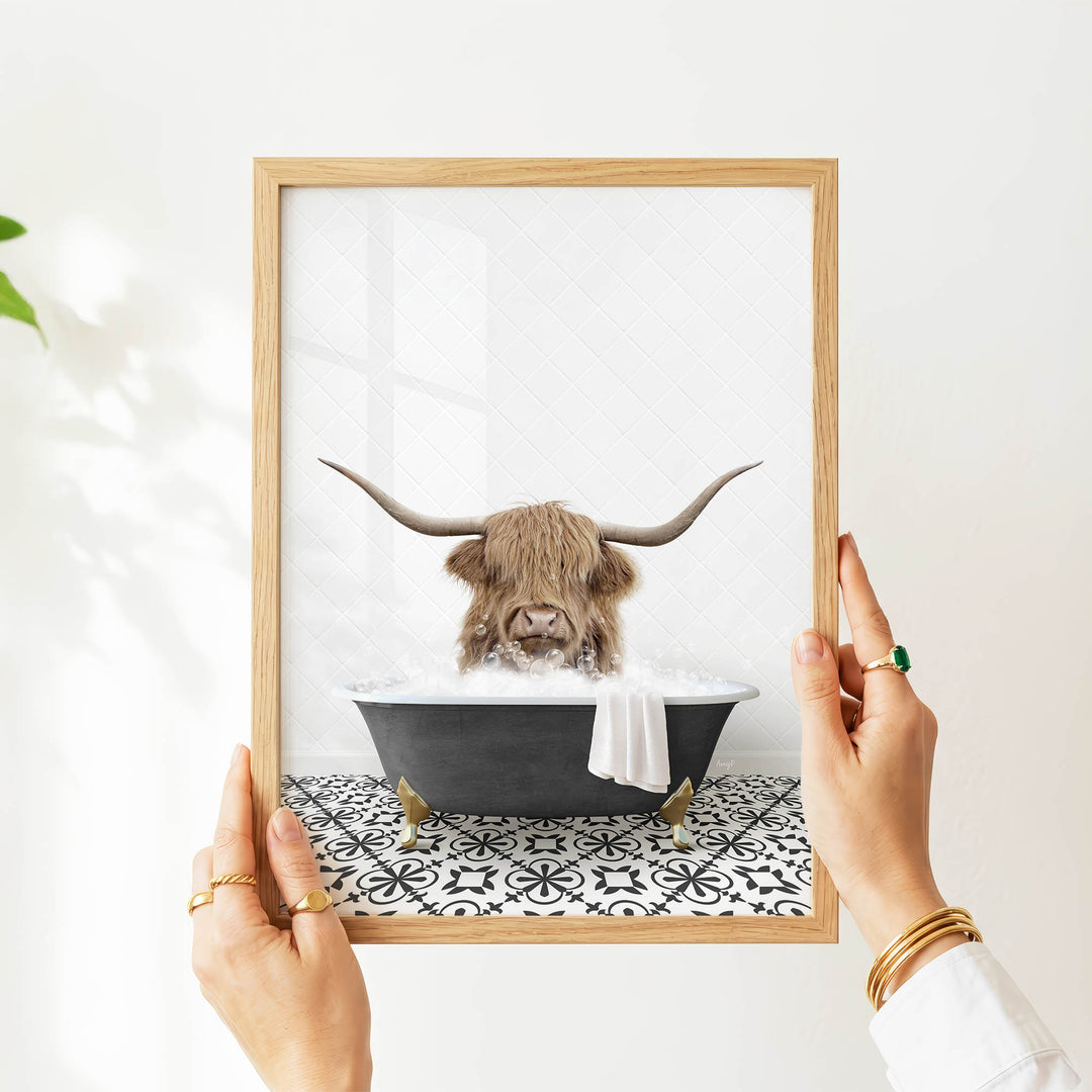 A person's hands are holding a framed picture of a horned animal, likely a yak or a yak, sitting in a bathtub filled with water.