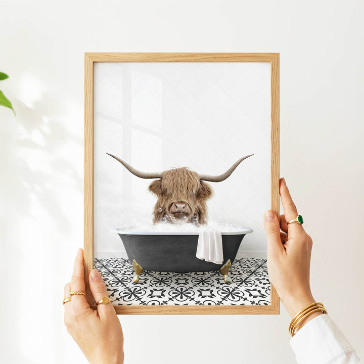 A person's hands are holding a framed picture of a horned animal, likely a yak or a yak, sitting in a bathtub filled with water.