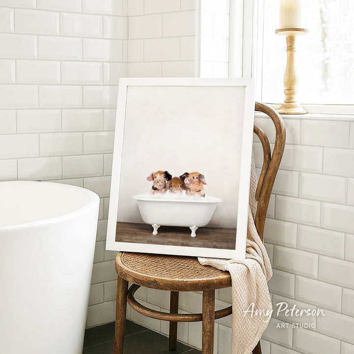 A framed photograph of three small dogs sitting in a white bathtub, with a wooden chair and a white tiled wall in the background.