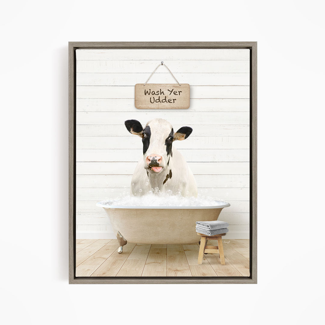 A black and white cow is sitting in a bathtub filled with water, with a wooden sign above it that says "Wash Yer Odder".