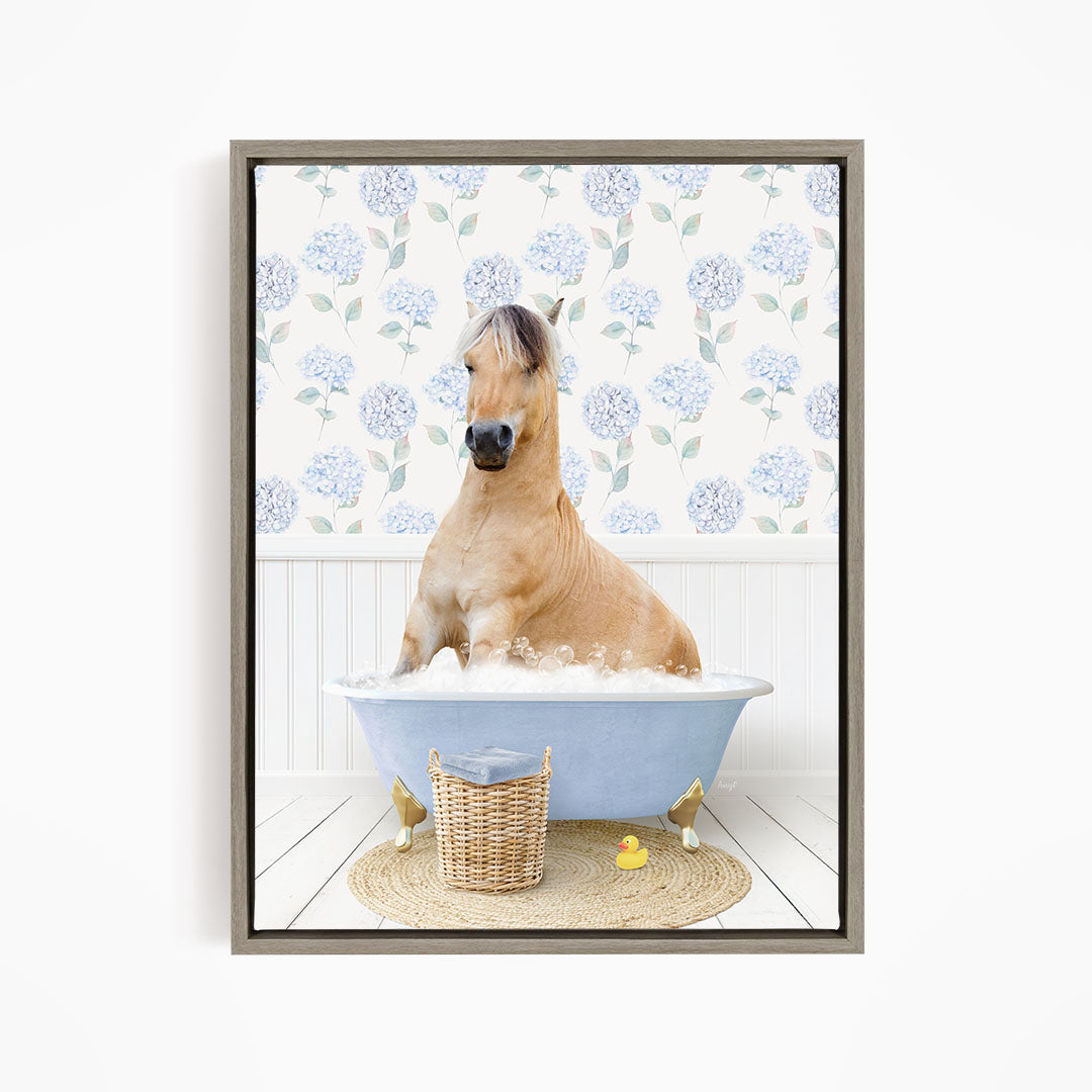 A light brown horse is sitting in a blue bathtub filled with water, surrounded by a wicker basket and rubber ducks.