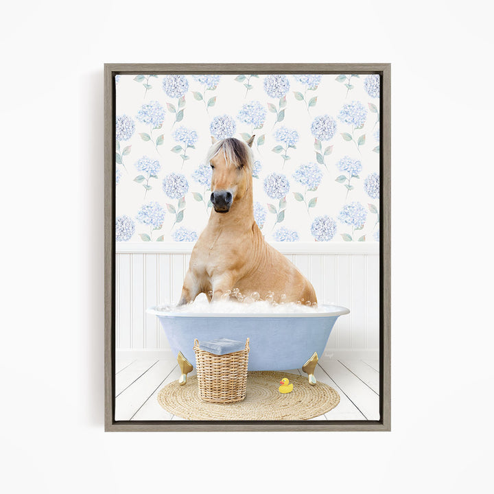 A light brown horse is sitting in a blue bathtub filled with water, surrounded by a wicker basket and rubber ducks.