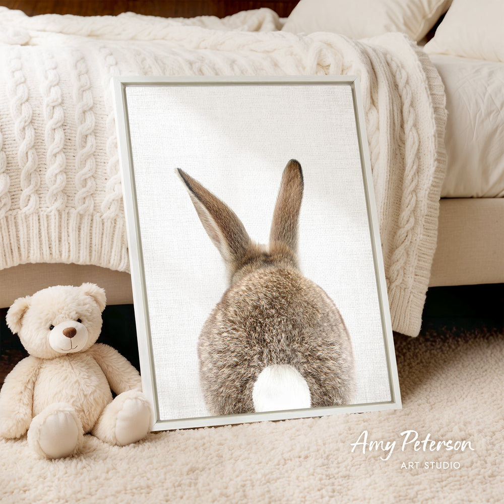 A framed image of a rabbit's back is displayed on a bed, accompanied by a teddy bear and a blanket.
