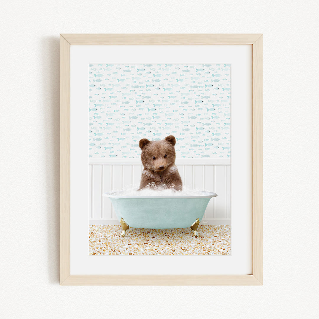 A small brown bear sitting in a light blue bathtub filled with bubbles, surrounded by a patterned wall and a beige floor.