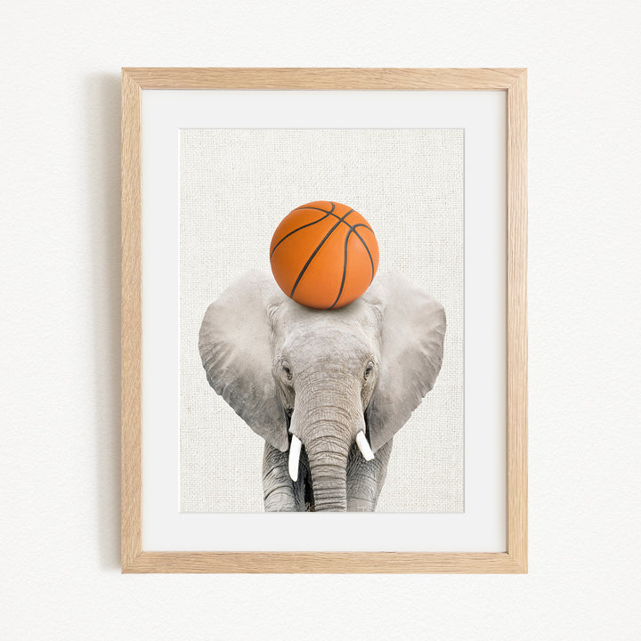 A gray elephant balances an orange basketball on its head, creating a playful and whimsical scene.
