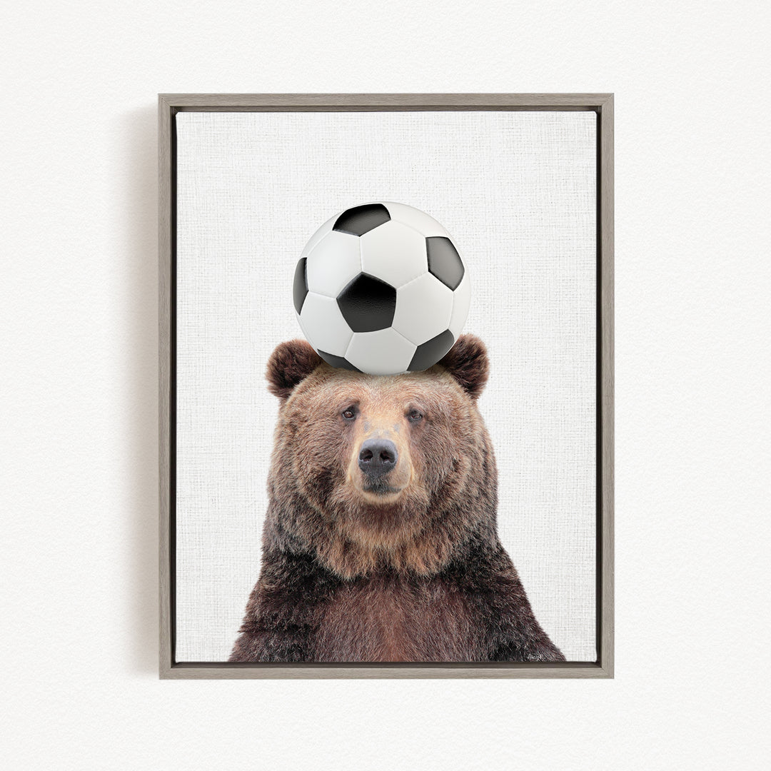 A brown bear balancing a soccer ball on its head.