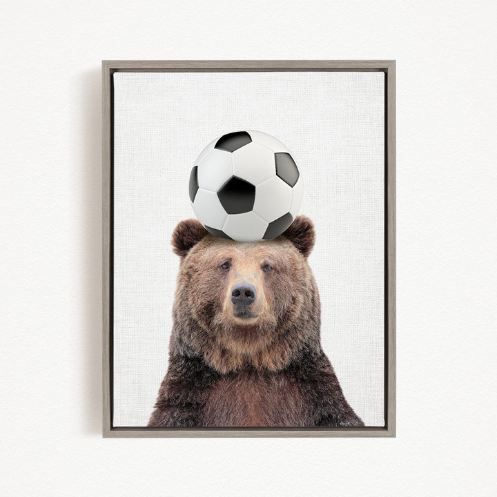 A brown bear balancing a soccer ball on its head.