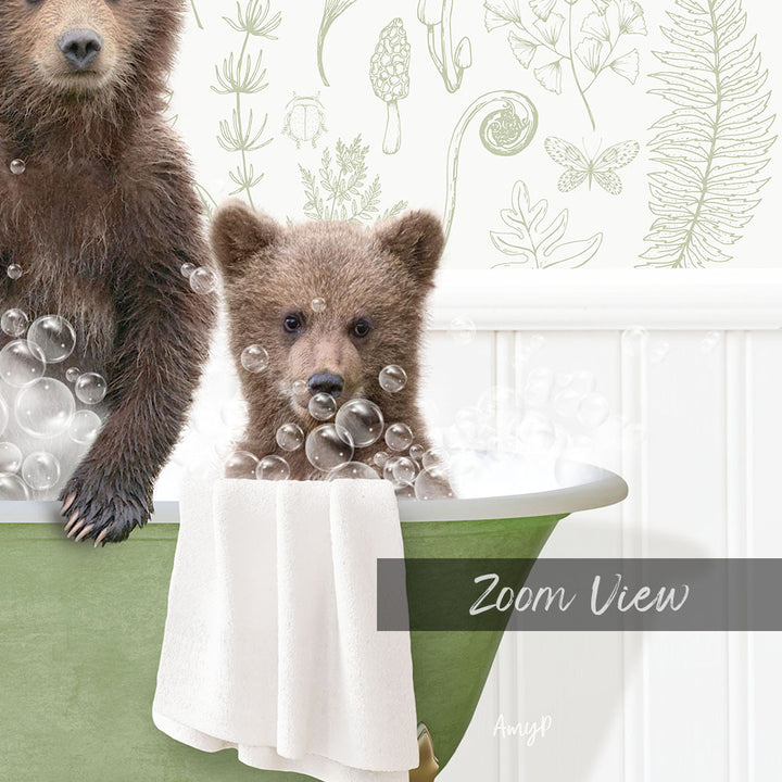 A baby bear sitting in a bathtub filled with bubbles, with a towel draped over the side of the tub.