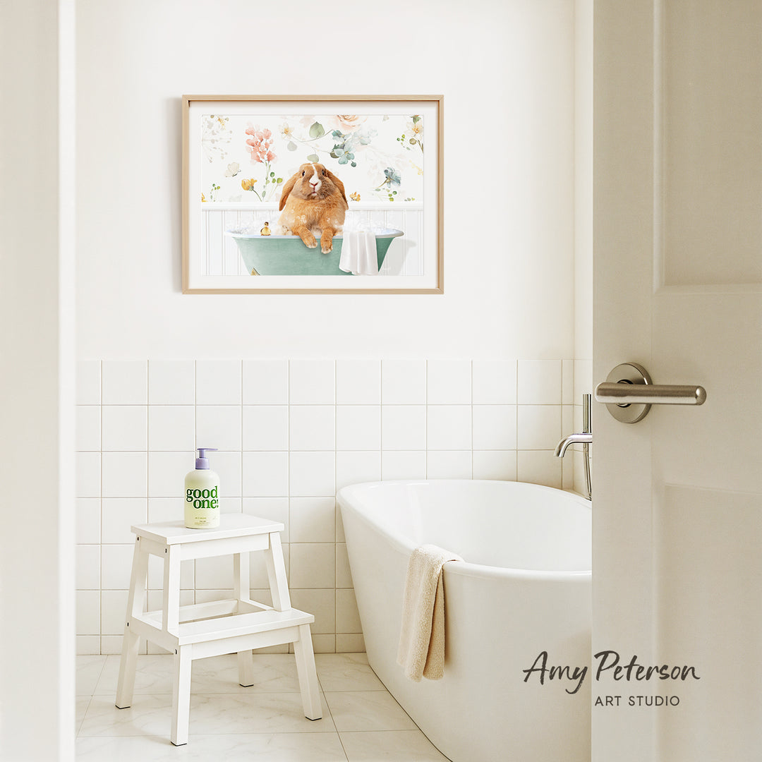 A framed painting of a dog sitting in a bathtub is hanging on the wall above a white bathtub in a bathroom.