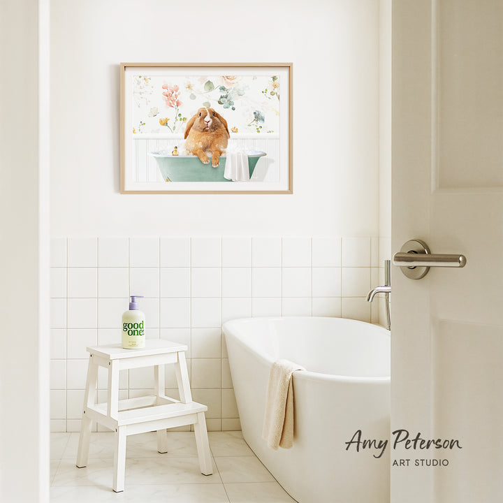A framed painting of a dog sitting in a bathtub is hanging on the wall above a white bathtub in a bathroom.