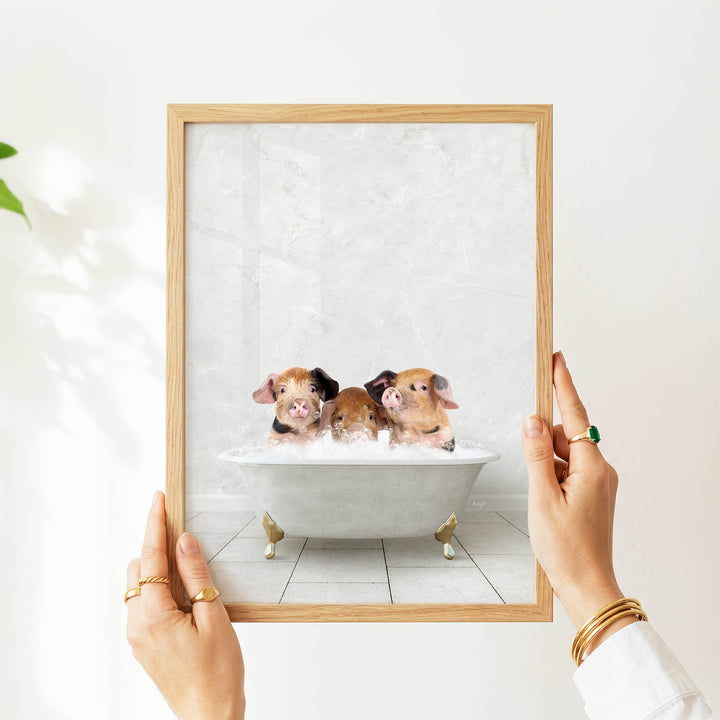 A person's hands are holding a framed picture of three adorable baby pigs sitting in a bathtub.