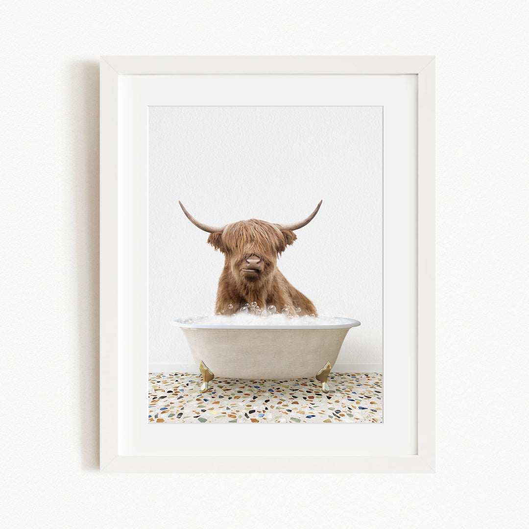 A brown Highland cow with large horns is sitting in a white bathtub filled with water, creating a whimsical and playful scene.