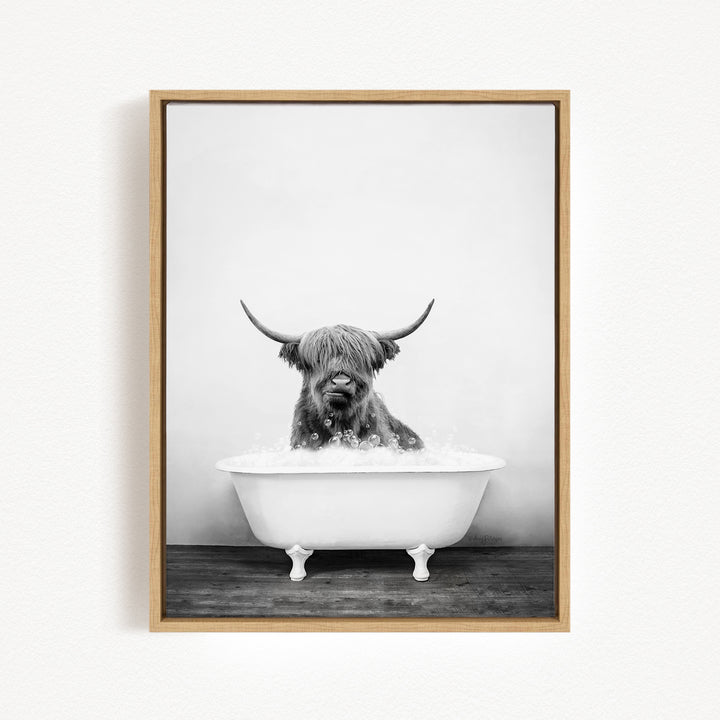 A black and white photograph of a Highland cow sitting in a bathtub filled with water.