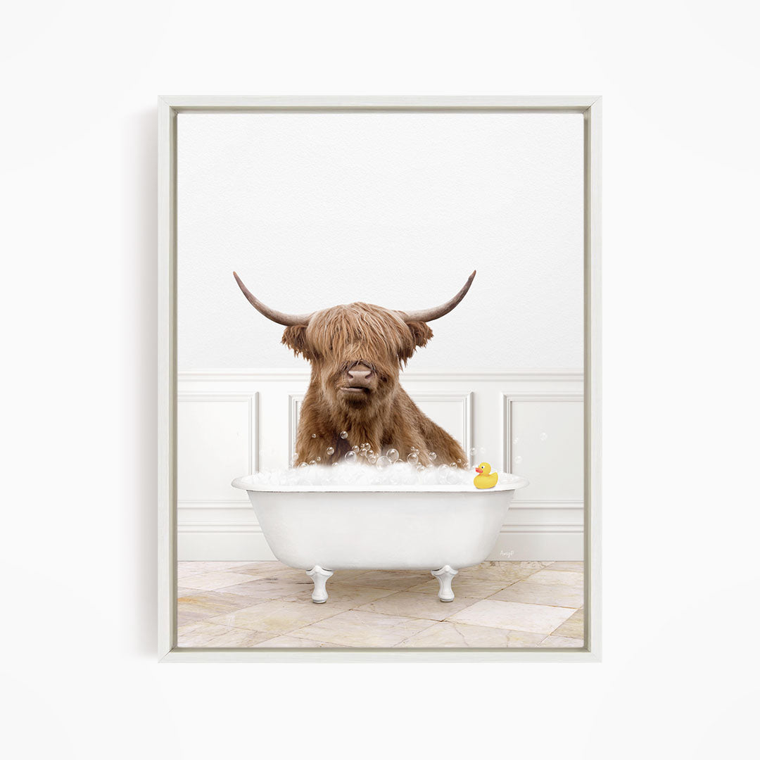 A brown cow with long horns is sitting in a white bathtub filled with water, with a yellow rubber duck floating in the tub.