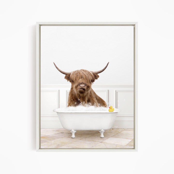 A brown cow with long horns is sitting in a white bathtub filled with water, with a yellow rubber duck floating in the tub.