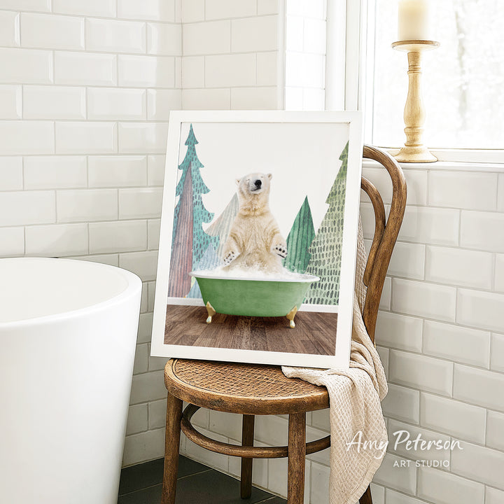 A framed image of a polar bear sitting in a green bathtub, surrounded by Christmas trees, is displayed on a wooden chair in a bathroom setting.