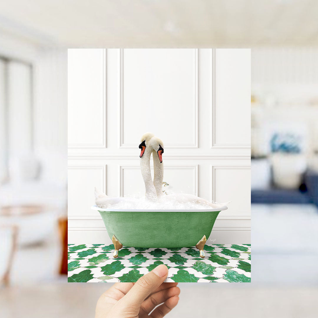 A hand holds up a framed photograph of a white swan sitting in a green bathtub filled with bubbles, with a blurred background suggesting a bathroom setting.