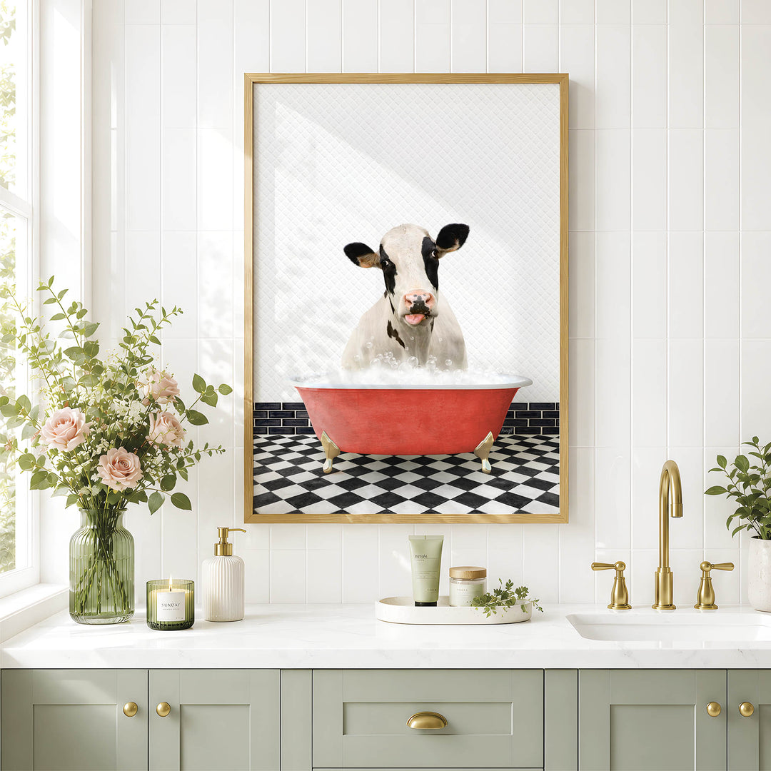 a bathroom with a framed picture of a cow sitting in a red bathtub, surrounded by flowers and greenery.