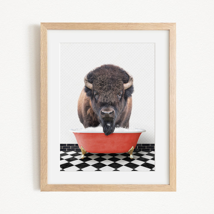 A buffalo with large horns is standing in a red bathtub, with a black and white checkered floor beneath it.