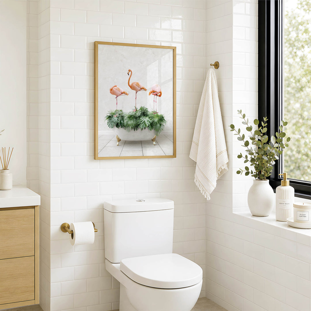 a bathroom with a white toilet, a framed picture of three pink flamingos in a green plant, a towel rack with a white towel, and a window with greenery outside.