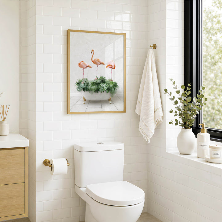 a bathroom with a white toilet, a framed picture of three pink flamingos in a green plant, a towel rack with a white towel, and a window with greenery outside.