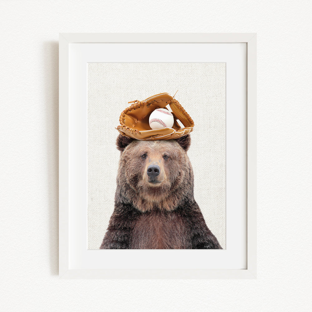 A brown bear wearing a baseball glove on its head, with a baseball resting on top of the glove.