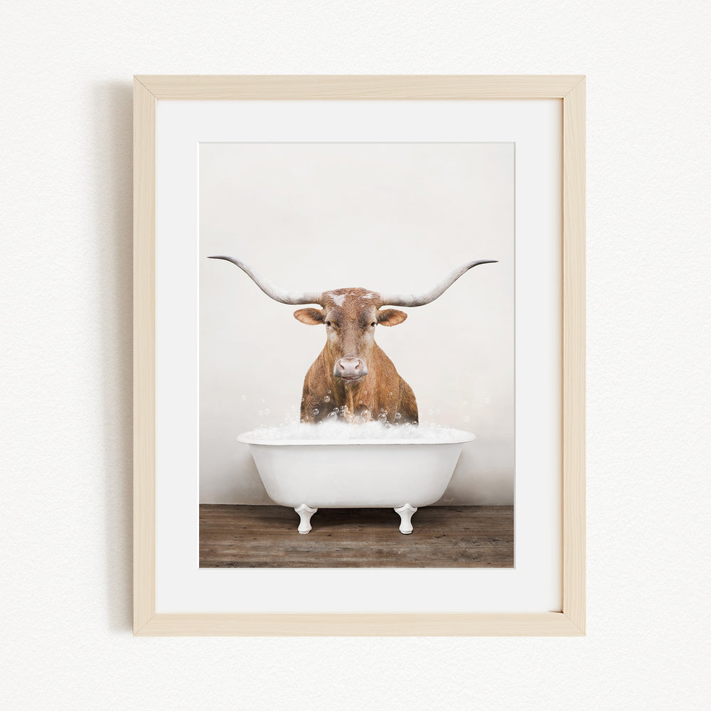 A brown cow with large horns is standing in a white bathtub filled with water, creating a whimsical and humorous scene.