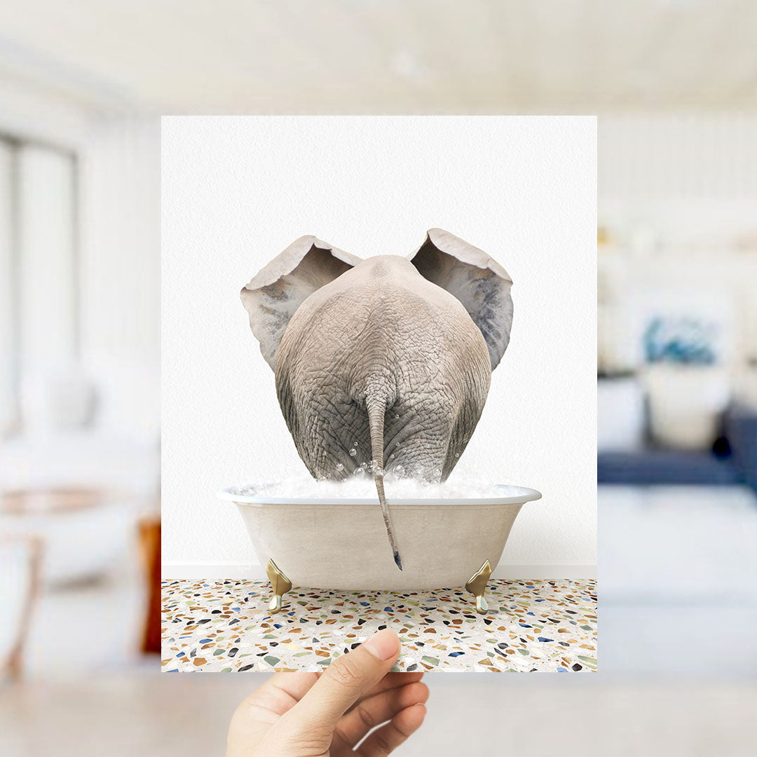 A hand holds up a framed image of an elephant standing in a bathtub filled with water, creating a whimsical and playful scene.