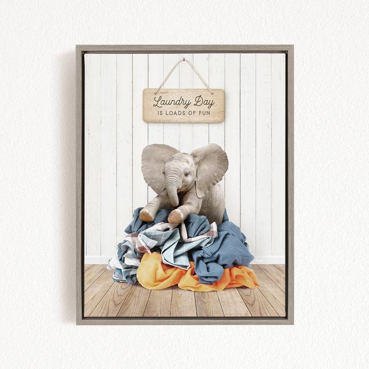 A framed image of a stuffed elephant sitting on a pile of laundry, with a wooden sign above it that says "Laundry Day is loads of fun".