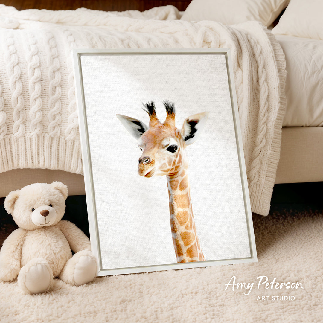 A framed image of a giraffe is displayed on a white bedspread, accompanied by a teddy bear on the floor.