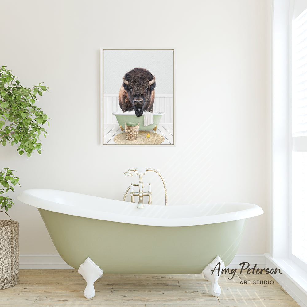A framed image of a buffalo is displayed on the wall above a green clawfoot bathtub in a bright, minimalist bathroom.