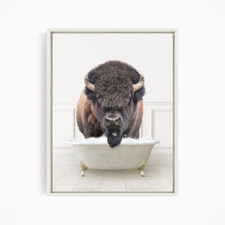 A buffalo with a long beard is standing in a white bathtub filled with water, looking directly at the camera.
