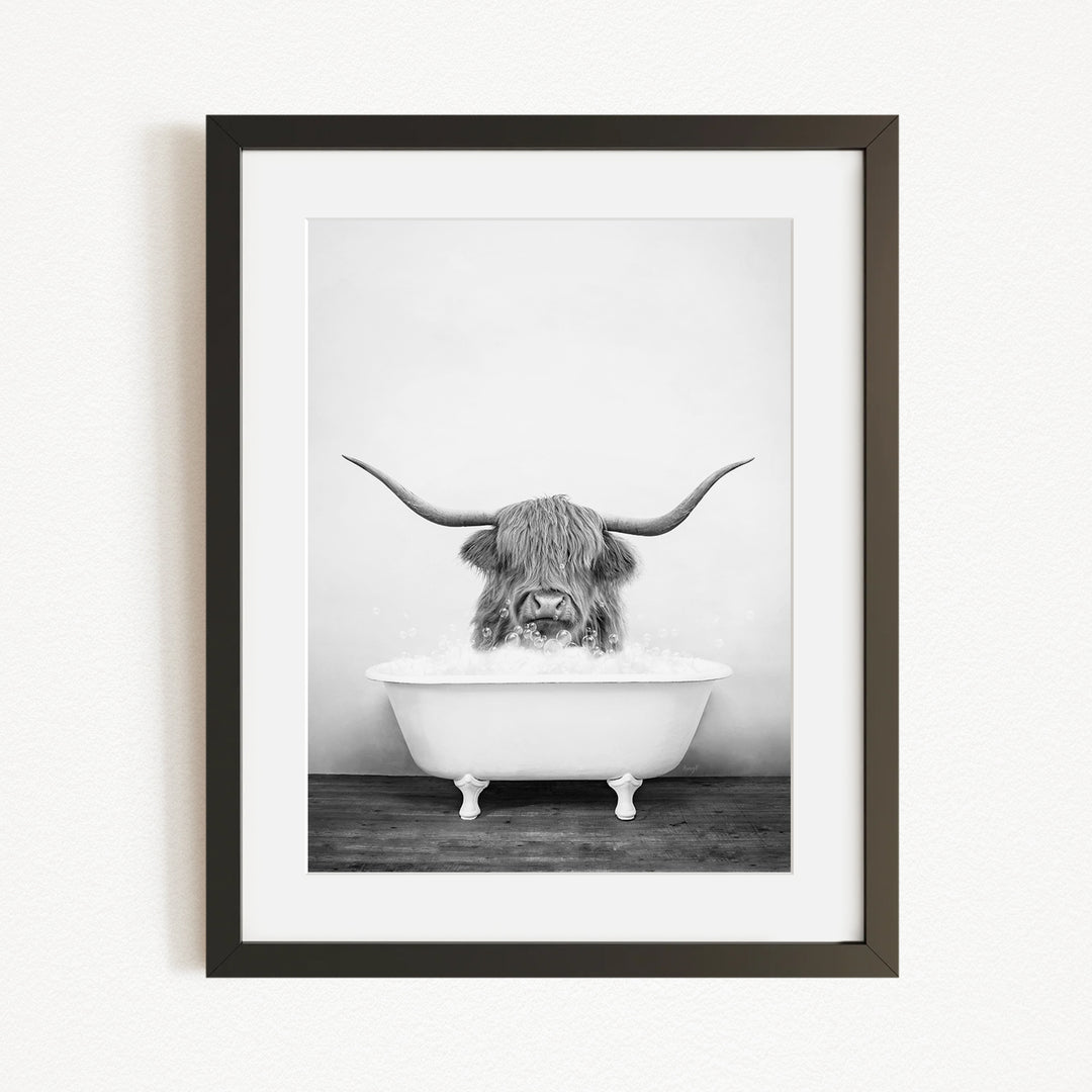 A black and white photograph of a Highland cow with long horns sitting in a bathtub.
