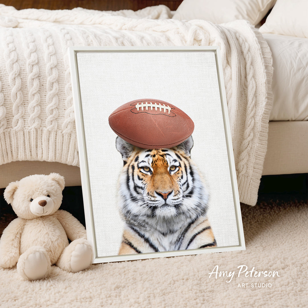 A framed print of a tiger wearing a football on its head is displayed on a bed, with a teddy bear next to it.