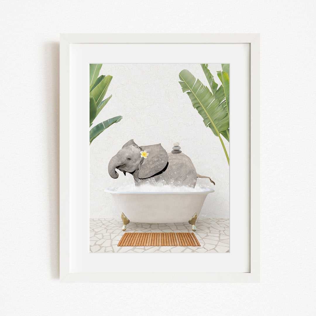 A framed image depicting a gray elephant sitting in a white bathtub, surrounded by green leaves and a wooden mat on the floor.